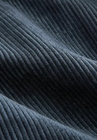 Närbild av mörkblå kordfløyeltyg som visar texturerade, parallella vertikala åsar och mjuka veck.