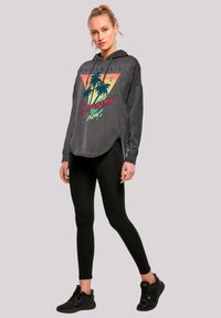 Gray hooded sweatshirt with a colorful palm tree graphic, paired with black leggings and black sneakers. Features a relaxed fit and side slits.
