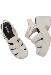 Sandali platform bianchi e lucidi con design a cinturini, caratterizzati da ritagli orizzontali e verticali, e una soletta nera a contrasto con branding.