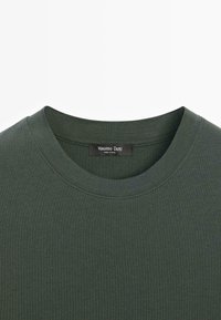 T-shirt di cotone verde scuro con scollo rotondo e maniche corte. Presenta una texture sottile e un'etichetta con scritto "Massimo Dutti" all'interno del collo.