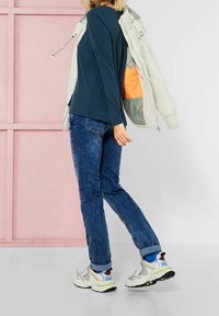 Mörk teal långärmad topp, ljus jacka med orange insidan, blå jeans och kraftiga flerfärgade sneakers. Enkelt, avslappnat outfit.