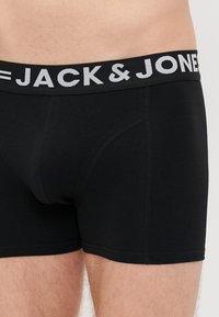Mustat puuvillabokserit, joissa on istuva muotoilu ja brändättömän joustovyön, jossa on valkoiset "JACK & JONES" -kirjaimet.