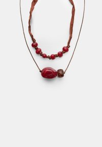 Naszyjniki z czerwonych korali z brązową wstążką i sznurkiem. Jeden z nich ma błyszczące czerwone kamienie, a drugi gładki owalny wisiorek.