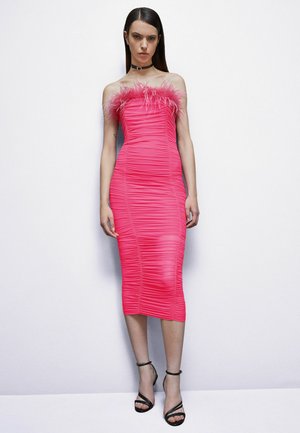 Abito rosa Ruché con rifinitura in piume a spalle scoperte, silhouette aderente, lunghezza al ginocchio, abbinato a décolleté neri con cinturino alla caviglia.