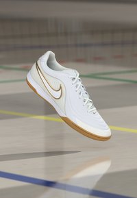 Λευκό αθλητικό παπούτσι Nike με υφή σχεδίου, χρυσές λεπτομέρειες και σόλα καραμέλας. Διαθέτει δέσιμο με κορδόνια και εξέχον λογότυπο Swoosh.