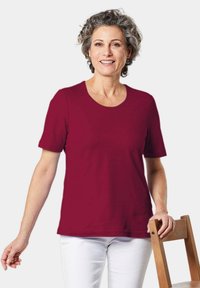 Bordeaux t-shirt met korte mouwen en een ronde hals, gemaakt van zachte stof, gecombineerd met witte broek, tegen een eenvoudige witte achtergrond.