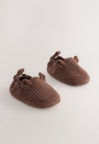 Chaussons en velours côtelé marron avec une texture côtelée et une doublure douce. Ils présentent une forme arrondie et deux petites oreilles décoratives sur le dessus.
