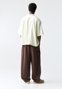 Chemise jaune clair à manches courtes avec des rayures verticales, associée à un pantalon ample marron ; présente un design minimaliste et une coupe décontractée.
