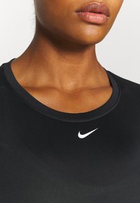 Schwarzes Sportoberteil mit Rundhalsausschnitt, glatter Textur und einem weißen Nike-Logo auf der Brust. Nahaufnahme, die sich auf den Hals und die Schultern konzentriert.