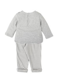 Top de manga larga gris con cierre de botón en la parte trasera, combinado con pantalones de cuadros en gris y blanco, con puños ajustados.