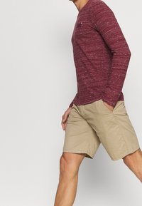 Röd marmorerad långärmad tröja med rund halsringning, matchad med beige knälånga shorts. Tyget verkar ha en texturerad yta med synliga sömmar.