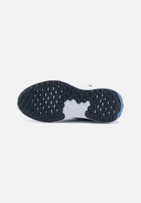 Semelle de sneaker avec une surface en caoutchouc noir présentant des motifs de traction circulaires et ovales, transitionnant vers le blanc à l'extrémité avec des accents bleus.