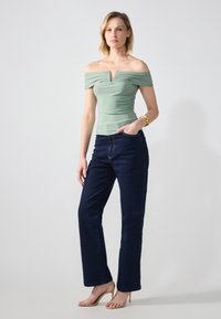 Top verde claro sin hombros con detalles fruncidos, combinado con jeans de pierna recta azul oscuro y tacones strap de color beige.