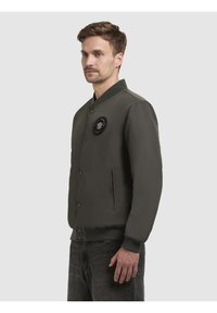 Hallide hall jacket sileda tekstuuriga, ribadega krae ja nööbikinnitus. Vasakul rinnal on ringikujuline logo.