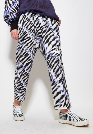 Loose-fitting, patterned pants in white with black and blue brushstroke designs, paired with white and black striped sneakers.