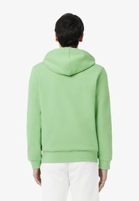 Sweat à capuche vert avec une coupe décontractée, capuche ajustable, poignets et ourlet côtelés, fabriqué en tissu doux et texturé. Vue arrière montrée.