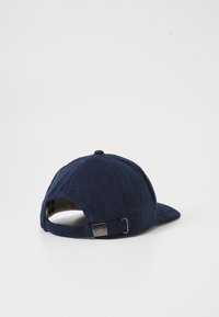 Marineblauwe corduroy baseballpet met een gebogen klep, een verstelbare band aan de achterkant en ton sur ton stiksel met een klein metalen logoaccent.