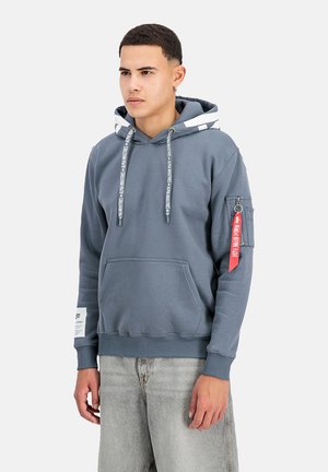 Sudadera de algodón gris con un bolsillo canguro en la parte frontal, cordones a rayas, un bolsillo con cremallera en el costado y una pestaña para llavero roja. Diseño de corte relajado.