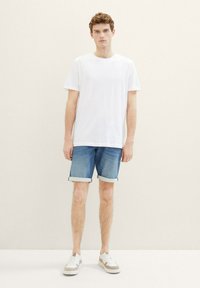 Camiseta blanca de manga corta combinada con pantalones cortos de mezclilla azules, con los dobladillos enrollados. Llevada con zapatillas blancas que tienen acentos en beige.