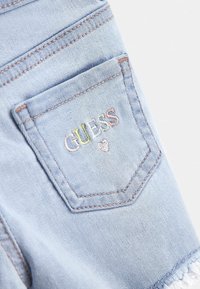 Jasnoniebieska kieszeń z dżinsu z haftem "GUESS" w pastelowych kolorach oraz małym serduszkiem poniżej napisu.