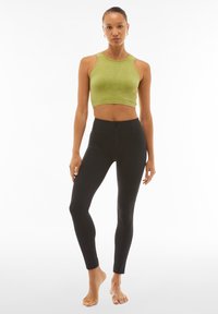 Crop top verde a coste abbinato a leggings neri a vita alta. Il top ha un colletto rotondo e un design senza maniche; i leggings hanno una texture liscia.