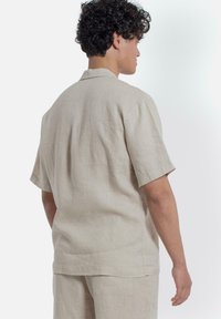 Beige linnen overhemd met korte mouwen, een relaxte pasvorm, een open kraag en een zachte textuur. Zichtbare stiksels aan de achterkant.