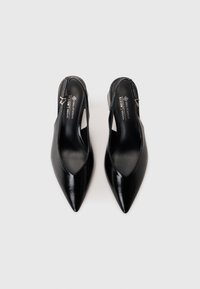 Scarpe slingback in ecopelle nera vegana con punta affusolata, lati intagliati e una piccola cinturino alla caviglia con hardware metallico. Finitura liscia.