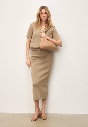 Dopasowany beżowy, krótki sweter z kołnierzykiem i przednimi kieszeniami, zestawiony z dopasowaną spódnicą midi oraz beżowymi butami na obcasie typu blok. Torba bezszwowa.