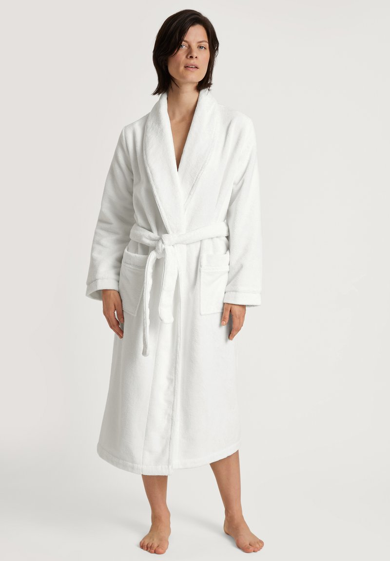 Witte badjas van badstof met lange mouwen, strikriem en twee voorzakken; knielengte met een zachte textuur en eenvoudig ontwerp.