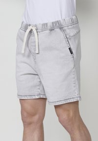Pantalones cortos de mezclilla gris con cintura elástica, cordón ajustable y bolsillos laterales. Presenta una sutil textura desvanecida y dobladillo cosido.
