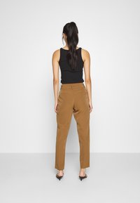 Pantalones marrones ajustados con una textura suave, combinados con una camiseta negra ceñida; el conjunto presenta una silueta elegante y un diseño minimalista.