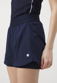 Pantalones cortos deportivos en color azul marino con una cinturilla ancha, hechos de tejido ligero. Presenta un logo blanco y un diseño en capas con pantalones cortos interiores.