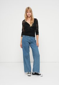 Zwarte kanten top met lange mouwen en een V-hals, gecombineerd met lichtblauwe wijde jeans en zwarte canvas sneakers.