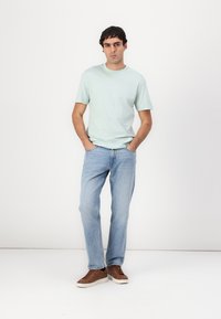 Lys mintgrøn bomulds T-shirt, afslappet pasform, korte ærmer; parret med lyseblå denimjeans og brune casual sneakers.