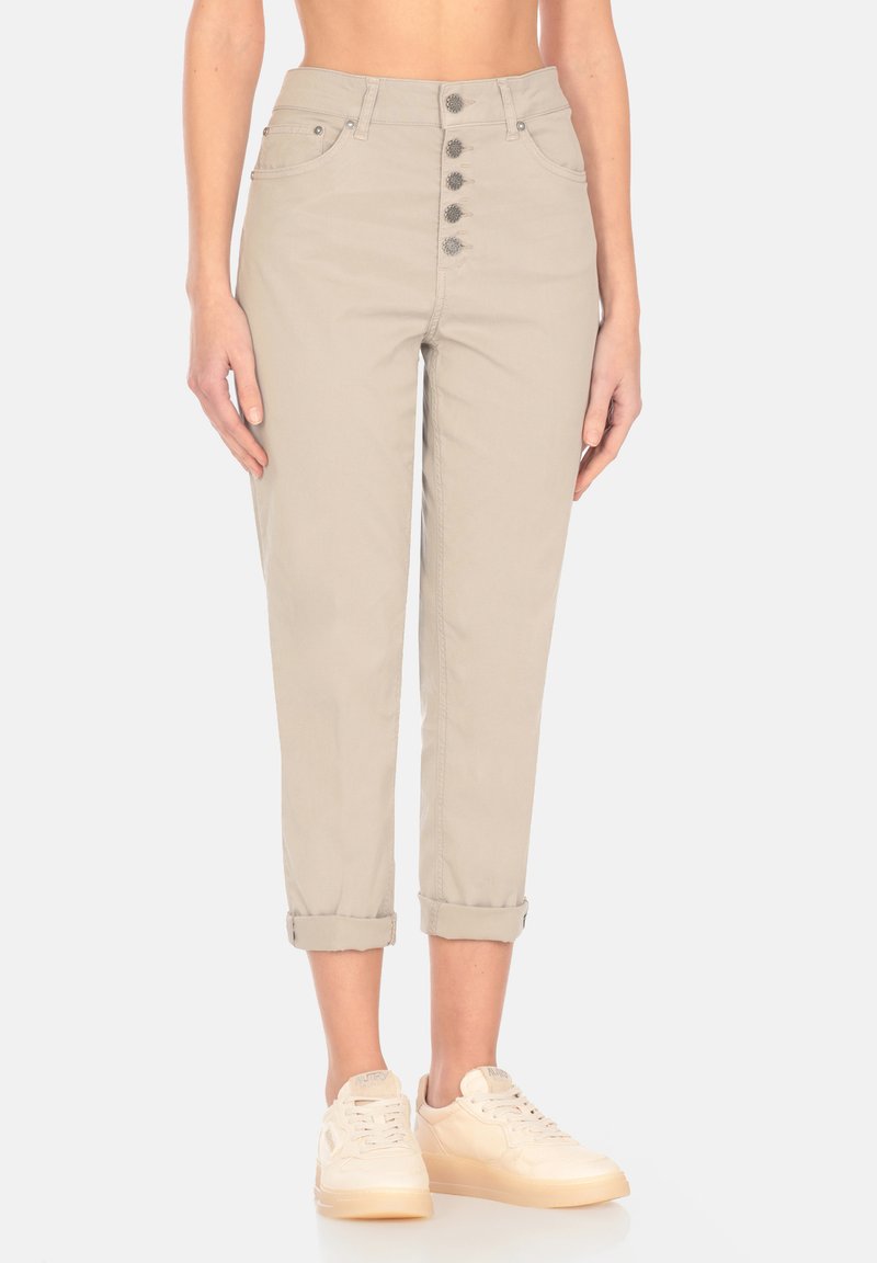 Pantaloni beige a vita alta con orli arrotolabili, chiusura frontale a cinque bottoni, tasche frontali e morbido tessuto di cotone. Abbinati a sneakers chiare.