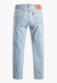 Jean en denim bleu clair coupe droite, deux poches arrière avec surpiqûres, un patch marque en cuir marron et une étiquette en tissu rouge sur la poche droite.