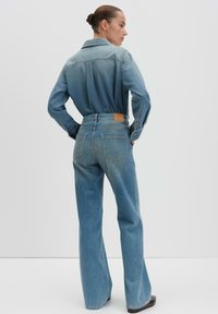 Ensemble en denim bleu clair composé d'une chemise et d'un jean. La chemise est dotée d'un col et de poignets à boutons ; le jean a une taille mi-haute et une coupe évasée.