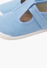 Scarpe in tela azzurra chiara con tomaia texturizzata, caratterizzate da un design a T e una suola in gomma bianca.