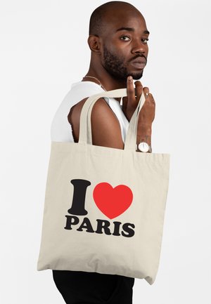 Borsa tote in canvas beige con "I ❤️ PARIS" in caratteri neri e rossi in grassetto. Presenta manici robusti e un design semplice e pulito.