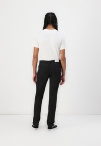 Black trousers with a straight fit, featuring a smooth texture and a simple design. Paired with a plain white t-shirt and black sneakers.