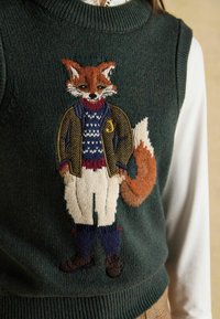 Zaļš adīts žakets ar izstrādātu lapsas izšuvumu, kas valkā jaku, rakstainu džemperi un bikses. Ribota apkakle un apakšmalas.