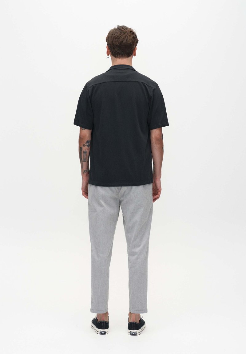 Schwarzes kurzärmliges Hemd, lässige Passform, mit weicher Textur. Kombiniert mit hellgrauen, taillierten Hosen und schwarzen Schuhen mit weißen Sohlen.