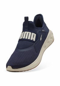 Sneakers navy senza lacci con tomaia in rete testurizzata, logo bianco prominente sulla fascia e suola beige chiaro con un motivo di battistrada in gomma.