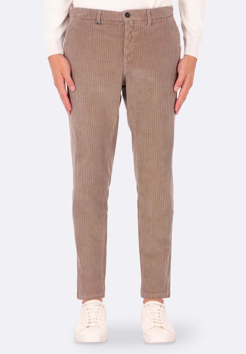 Pantaloni in velluto a coste marrone con righe verticali, dotati di chiusura frontale con bottone e zip, e tasche anteriori. Abbinati a sneaker bianche.