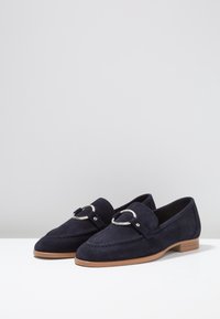 Mocassini in suede blu navy con tacco piatto, dotati di una fibbia decorativa in metallo argentato e dettagli di cucitura sulla parte superiore.