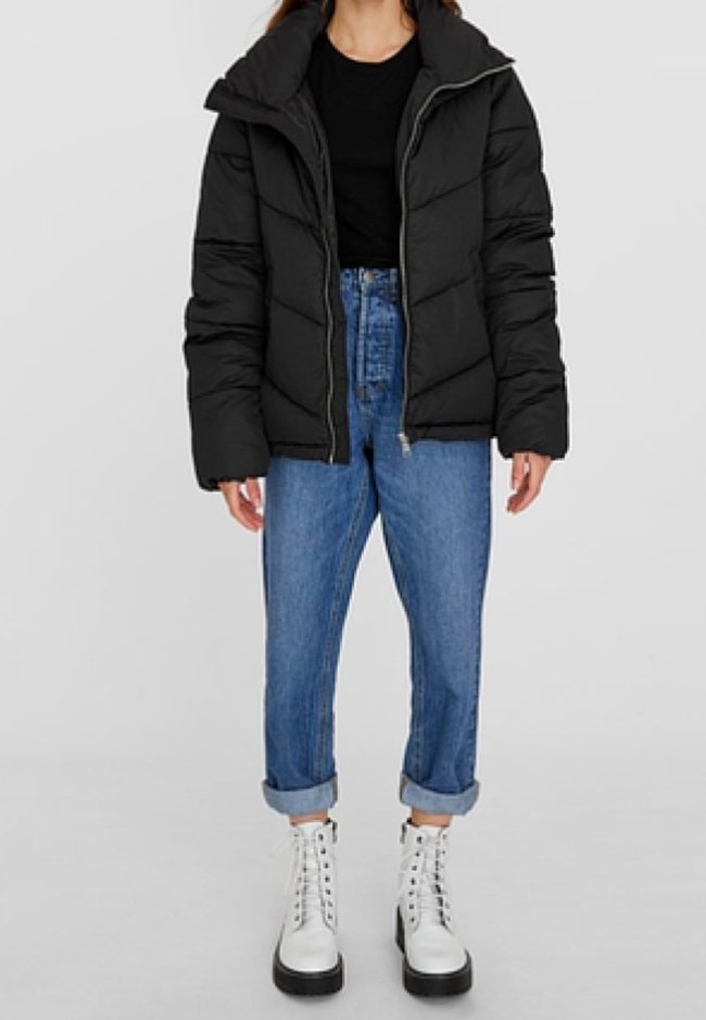 Czarna kurtka puchowa z zapięciem na zamek i kapturem, w połączeniu z jasnoniebieskimi dżinsami z podwiniętymi mankietami oraz białymi wiązanymi butami. Gładka tekstura.