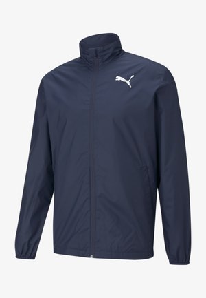 Kurtka przeciwwiatrowa Puma w kolorze granatowym, z wysokim kołnierzem, pełnym zamkiem, długimi rękawami i białym logo na lewej piersi.