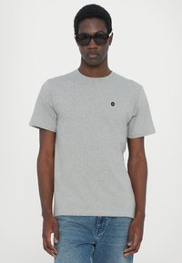 Tricou gri din bumbac cu mâneci scurte, guler circular și un mic logo negru pe piept. Poartă-l cu blugi denim albaștri și ochelari de soare.