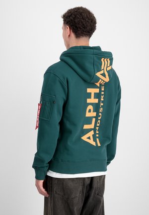 Felpa con cappuccio verde caratterizzata da un grande logo arancione "ALPHA INDUSTRIES" sul retro, con una tasca con zip sul manica sinistra.