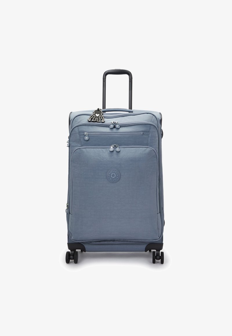 Ljusblå hård resväska med två framdragare, utdragbart handtag, svarta hjul och en svart karaktärsberlock fäst vid dragkedjan.